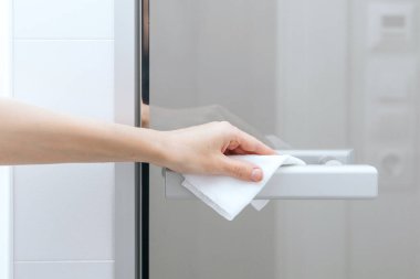 Cam kapı kollarını antiseptik ıslak mendille temizliyorum. Hastane ve kamusal alanlarda korona virüsüne karşı korunma yüzeylerini sterilize edin. Kadın eli temizlik için havlu kullanıyor.