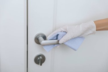 Beyaz eldivenli, mavi mendilli kapı kolu. Hastane ve kamusal alanlarda korona virüsüne karşı korunma yüzeylerini sterilize edin. Kadın eli temizlik için havlu kullanıyor.