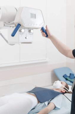 Doktor sedyede yatan hastanın röntgenini çekiyor. Hastane radyoloji odası. Teknisyen röntgen cihazını ayarlıyor. Yatakta yatan kadın modern klinikte göğüs, kalp ve akciğerleri tarıyor.