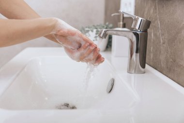 Akan su musluğunun altında ellerini yıkamak. Hijyen konsepti el detayı. Corona virüsünün önlenmesi için sabunla ellerini ovuşturmak, korona virüsünü halka yaymayı durdurmak için hijyen. Ya da umumi tuvalette.