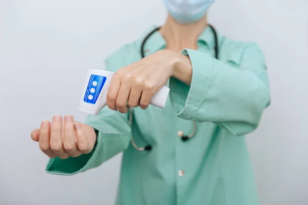 Temperature measurement gun in doctor hands. Close-up shot of doctor wearing protective surgical mask ready to use infrared isometric thermometer gun to check body temperature for virus symptoms — Stock Photo, Image