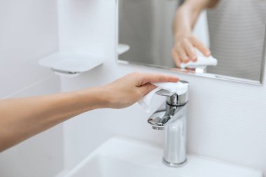 Lavabo musluğunu mikrofiber bezle temizliyorum. Hastane ve kamusal alanlarda korona virüsüne karşı korunma yüzeylerini sterilize edin. Islak mendil kullanan kadın eli. Banyoyu temizliyorum.