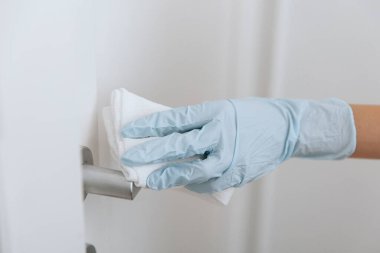 Siyah kapı kollarını antiseptik ıslak mendille mavi eldivenlerle temizliyorum. Hastane ve kamusal alanlarda korona virüsüne karşı korunma yüzeylerini sterilize edin. Kadın eli temizlik için havlu kullanıyor.