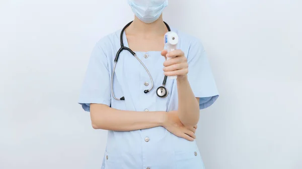 Medição de temperatura arma em mãos de médico. Close-up tiro do médico usando máscara cirúrgica protetora pronto para usar arma termômetro isométrico infravermelho para verificar a temperatura do corpo para os sintomas do vírus — Fotografia de Stock