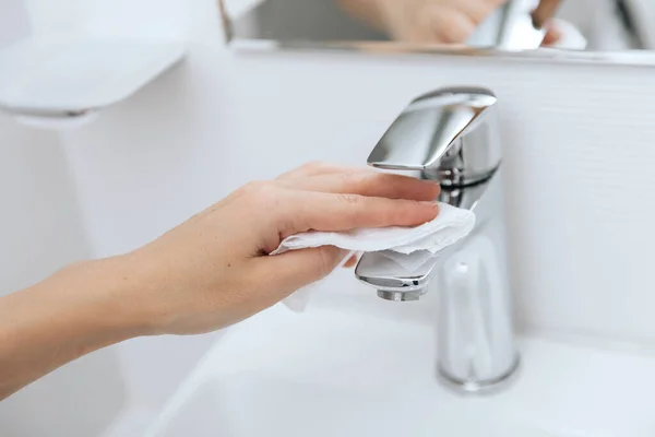 Limpieza del grifo del fregadero con un paño de microfibra. Desinfectar las superficies de prevención en los espacios hospitalarios y públicos contra el virus corona. Mano de mujer usando toallita húmeda. Limpieza del baño — Foto de Stock