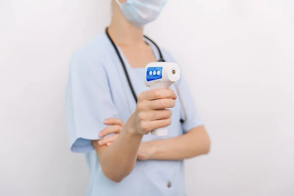 Temperatuurmeetpistool in doktershanden. Close-up shot van de arts met beschermende chirurgische masker klaar voor gebruik infrarood isometrische thermometer pistool om de lichaamstemperatuur te controleren op virussymptomen — Stockfoto