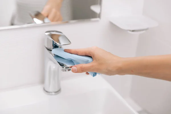 シンク蛇口をマイクロファイバークロスで清掃します。病院や公共スペースでコロナウイルスに対する表面の予防を衛生化します。ぬれたワイプで女性の手。浴室の掃除 — ストック写真