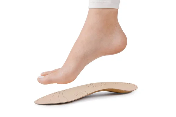 Medical insoles. Isolated orthopedic insoles on a white background. Treatment and prevention of flat feet and foot diseases. Foot care. Insole cutaway layers. Leg hanging over the insole — Stock Photo, Image