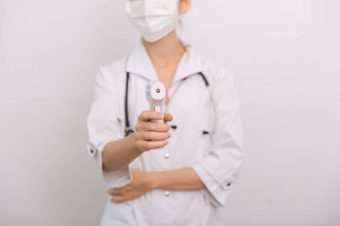 Sıcaklık ölçüm silahı doktorun elinde. Doktorun koruyucu cerrahi maske takıp vücut ısısını kontrol etmek için kızılötesi izometrik termometre tabancası kullanmaya hazır olduğu yakın çekim.