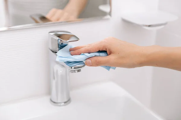 एक माइक्रोफ़ाइबर कपड़े से सिंक नल की सफाई। कोरोना वायरस के खिलाफ अस्पताल और सार्वजनिक स्थानों में सतहों की रोकथाम को स्वच्छ बनाएं। गीले पोंछे का उपयोग कर महिला हाथ। बाथरूम की सफाई — स्टॉक फ़ोटो, इमेज