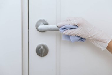 Beyaz eldivenli, mavi mendilli kapı kolu. Hastane ve kamusal alanlarda korona virüsüne karşı korunma yüzeylerini sterilize edin. Kadın eli temizlik için havlu kullanıyor.
