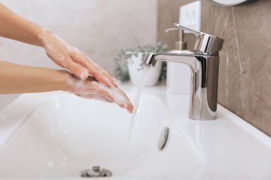Akan su musluğunun altında ellerini yıkamak. Hijyen konsepti el detayı. Corona virüsünün önlenmesi için sabunla ellerini ovuşturmak, korona virüsünü halka yaymayı durdurmak için hijyen. Ya da umumi tuvalette.