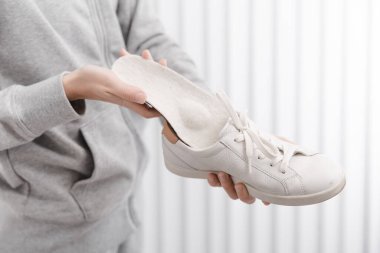Ortopedik tabanı evde ayakkabıya takan kadın. Spor kızı ortopedik insole 'u içeride takıyor, kapat. Ayak bakımı afişi. Düz Ayak Düzeltme. Ayak hastalıklarının tedavisi ve önlenmesi