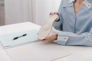 Doktor masada otururken taban tabanı tutuyor. Ortopedist tıbbi cihazı test ediyor. Ortopedik tabanlar. Ayak bakımı. Düz Ayak Düzeltme. Düztaban ve ayak hastalıklarının tedavisi ve önlenmesi