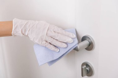 Beyaz eldivenli, mavi mendilli kapı kolu. Hastane ve kamusal alanlarda korona virüsüne karşı korunma yüzeylerini sterilize edin. Kadın eli temizlik için havlu kullanıyor.