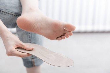 Kadın ortopedik insole 'u içeride takıyor, kapatın. Evde ayağının yanında taban tutan bir kız. Ortopedik tabanlar. Ayak bakımı afişi. Düz Ayak Düzeltme. Ayak hastalıklarının tedavisi ve önlenmesi