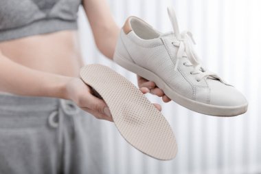 Ortopedik tabanı evde ayakkabıya takan kadın. Spor kızı ortopedik insole 'u içeride takıyor, kapat. Ayak bakımı afişi. Düz Ayak Düzeltme. Ayak hastalıklarının tedavisi ve önlenmesi