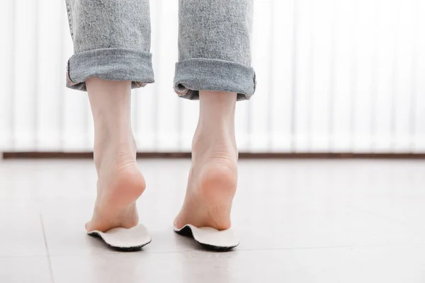 Kadın ortopedik insole 'u içeride takıyor, kapatın. Evde ayağının yanında taban tutan bir kız. Ortopedik tabanlar. Ayak bakımı afişi. Düz Ayak Düzeltme. Ayak hastalıklarının tedavisi ve önlenmesi