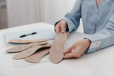 Doktor masada otururken taban tabanı tutuyor. Ortopedist tıbbi cihazı test ediyor. Ortopedik tabanlar. Ayak bakımı. Düz Ayak Düzeltme. Düztaban ve ayak hastalıklarının tedavisi ve önlenmesi