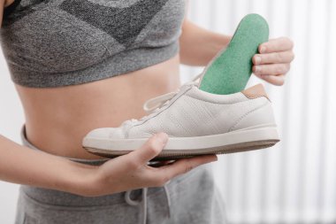 Spor giyimli, spor ayakkabılı, tabanlı, spor ayakkabılı bir kadın. Ortopedik tabanı ayakkabıya takan kadın. Ayak bakımı afişi. Düz Ayak Düzeltme