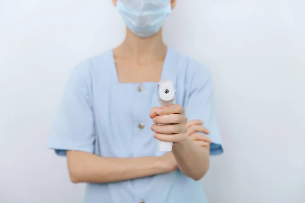 Όπλο μέτρησης θερμοκρασίας σε χέρια γιατρού. Κοντινό πλάνο του γιατρού φορώντας προστατευτική χειρουργική μάσκα έτοιμη να χρησιμοποιήσει υπέρυθρο ισομετρικό όπλο θερμόμετρο για να ελέγξει τη θερμοκρασία του σώματος για συμπτώματα του ιού — Φωτογραφία Αρχείου