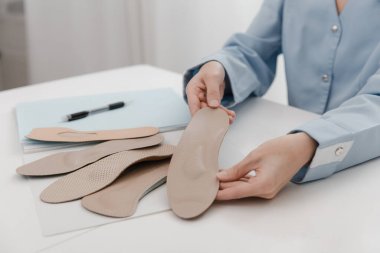 Doktor masada otururken taban tabanı tutuyor. Ortopedist tıbbi cihazı test ediyor. Ortopedik tabanlar. Ayak bakımı. Düz Ayak Düzeltme. Düztaban ve ayak hastalıklarının tedavisi ve önlenmesi