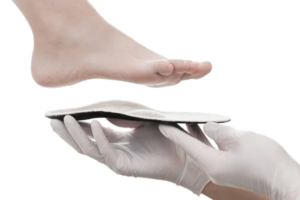 Ортопедическая стелька изолирована на белом фоне. Руки в резиновых перчатках держат ортопедическую стельку. Уход за ногами, комфорт для ног. Врач-ортопед проверяет медицинское устройство. Коррекция плоских ног — стоковое фото