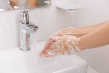 Akan su musluğunun altında ellerini yıkamak. Hijyen konsepti el detayı. Corona virüsünün önlenmesi için sabunla ellerini ovuşturmak, korona virüsünü halka yaymayı durdurmak için hijyen. Ya da umumi tuvalette.