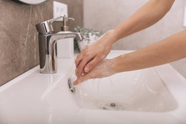 Akan su musluğunun altında ellerini yıkamak. Hijyen konsepti el detayı. Corona virüsünün önlenmesi için sabunla ellerini ovuşturmak, korona virüsünü halka yaymayı durdurmak için hijyen. Ya da umumi tuvalette.