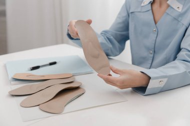 Doktor masada otururken taban tabanı tutuyor. Ortopedist tıbbi cihazı test ediyor. Ortopedik tabanlar. Ayak bakımı. Düz Ayak Düzeltme. Düztaban ve ayak hastalıklarının tedavisi ve önlenmesi