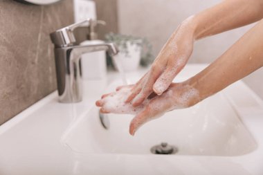 Akan su musluğunun altında ellerini yıkamak. Hijyen konsepti el detayı. Corona virüsünün önlenmesi için sabunla ellerini ovuşturmak, korona virüsünü halka yaymayı durdurmak için hijyen. Ya da umumi tuvalette.