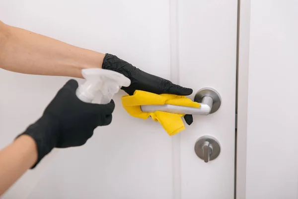 Cleaning door handle with yellow wipe in black gloves and sanitizer spray. Disinfection in hospital and public spaces against corona virus. Woman hand using towel for cleaning — Stock Photo, Image