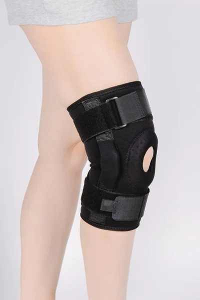 Térd támogatás Brace lábon elszigetelt fehér háttér. Rugalmas ortopédiai ortopédia. Anatómiai fogszabályzó térdmerevségre, sérülésekre és fájdalomra. Védő térdízületi kötés. Trauma, rehabilitáció — Stock Fotó