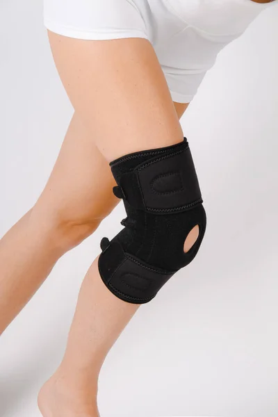 Térd támogatás Brace lábon elszigetelt fehér háttér. Rugalmas ortopédiai ortopédia. Anatómiai fogszabályzó térdmerevségre, sérülésekre és fájdalomra. Védő térdízületi kötés. Trauma, rehabilitáció — Stock Fotó