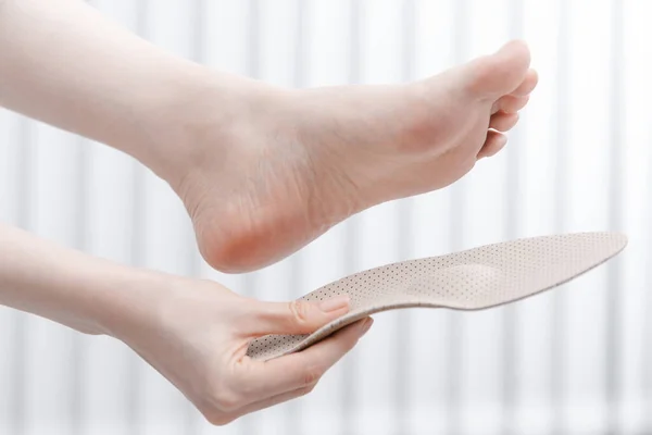 Woman fitting orthopedic insole indoors, close up. Girl holding an insole next to foot at home. Orthopedic insoles. Foot care banner. Flat Feet Correction. Treatment and prevention of foot diseases