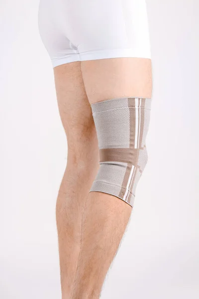 Knee Support Brace on leg isolated on white background. Elastic orthopedic orthosis. Anatomic braces for knee fixation, injuries and pain. Protective knee joint bandage sleeve. Trauma, rehabilitation