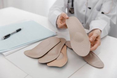 Doktor masada otururken taban tabanı tutuyor. Ortopedist tıbbi cihazı test ediyor. Ortopedik tabanlar. Ayak bakımı. Düz Ayak Düzeltme. Düztaban ve ayak hastalıklarının tedavisi ve önlenmesi
