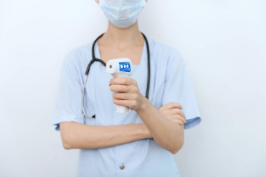 Sıcaklık ölçüm silahı doktorun elinde. Doktorun koruyucu cerrahi maske takıp vücut ısısını kontrol etmek için kızılötesi izometrik termometre tabancası kullanmaya hazır olduğu yakın çekim.