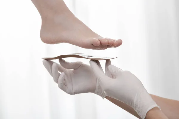 白い背景に整形外科のインソール.ゴム手袋の手は整形外科のインソールを保持します。足のケア、足の快適さ。整形外科医は医療機器をテストします。平らな足の修正 — ストック写真