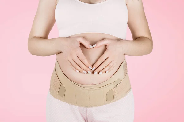 Pregnant woman belly in prenatal pregnancy maternity belt isolated on pink background. Orthopedic abdominal support waist, back, abdomen band. Belly Brace for pregnancy. Horizontal banner or poster