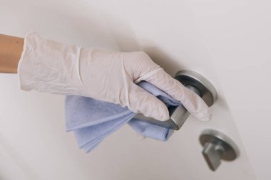 Beyaz eldivenli, mavi mendilli kapı kolu. Hastane ve kamusal alanlarda korona virüsüne karşı korunma yüzeylerini sterilize edin. Kadın eli temizlik için havlu kullanıyor.