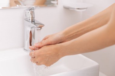 Akan su musluğunun altında ellerini yıkamak. Hijyen konsepti el detayı. Corona virüsünün önlenmesi için sabunla ellerini ovuşturmak, korona virüsünü halka yaymayı durdurmak için hijyen. Ya da umumi tuvalette.