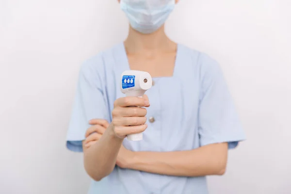 Temperatuurmeetpistool in doktershanden. Close-up shot van de arts met beschermende chirurgische masker klaar voor gebruik infrarood isometrische thermometer pistool om de lichaamstemperatuur te controleren op virussymptomen — Stockfoto