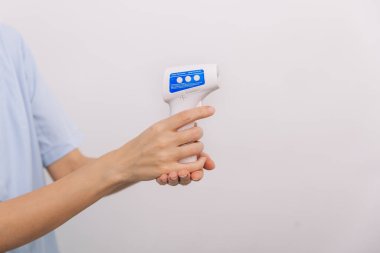 Sıcaklık ölçüm silahı doktorun elinde. Doktorun koruyucu cerrahi maske takıp vücut ısısını kontrol etmek için kızılötesi izometrik termometre tabancası kullanmaya hazır olduğu yakın çekim.