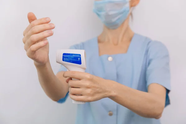 Temperatuurmeetpistool in doktershanden. Close-up shot van de arts met beschermende chirurgische masker klaar voor gebruik infrarood isometrische thermometer pistool om de lichaamstemperatuur te controleren op virussymptomen — Stockfoto