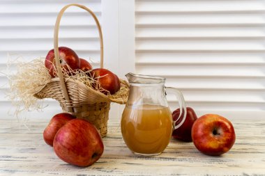 Sepetteki kırmızı elmalar ve tahta masadaki sürahide elma suyu.