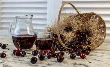 Kiraz ve kiraz suyu veya ahşap bir masada şarap, bir sürahi ve meyve suyu dolu bir bardak, kirazlı bir sepet.