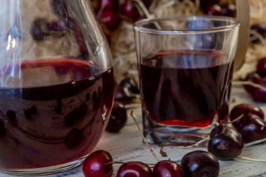 Kiraz ve kiraz suyu veya ahşap bir masada şarap, bir sürahi ve meyve suyu dolu bir bardak, kirazlı bir sepet.