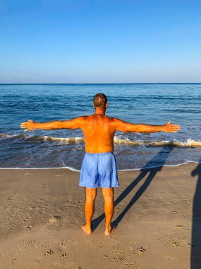 Bir adam spor yapmaya gider, deniz kıyısında egzersiz yapar.