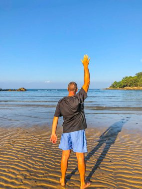 Bir adam spor yapmaya gider, deniz kıyısında egzersiz yapar.